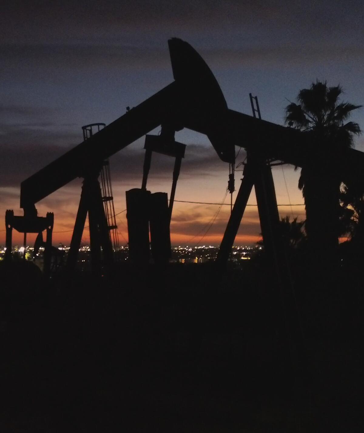 Oil derricks pump against a red sunset.