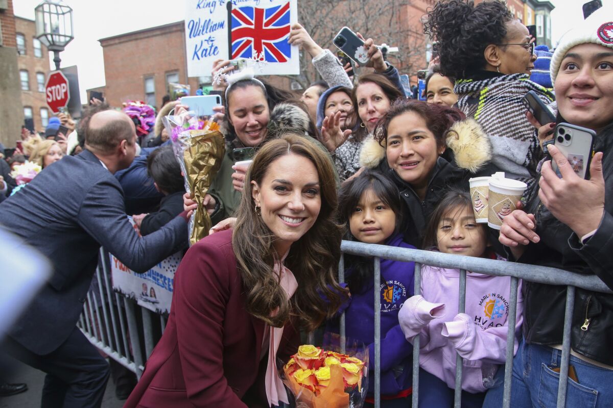 Britain's Kate, Princess of Wales poses for a photo with the crowd after a tour of Roca Thursday, Dec. 1, 2022, in Chelsea, Mass. Britain's Prince William greets people on the left. The Prince and Princess of Wales are making their first overseas trip since the death of Queen Elizabeth II in September. (AP Photo/Reba Saldanha, Pool)