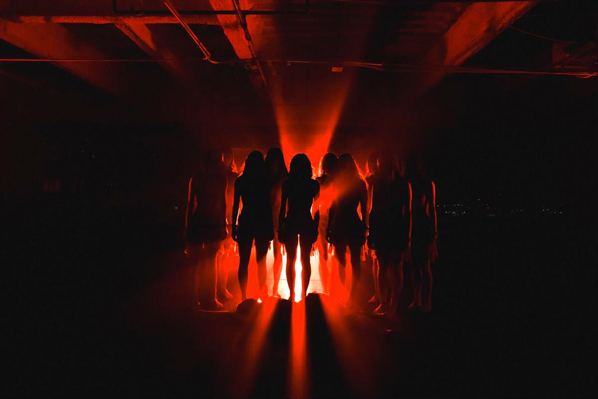 Shadows of women standing in a group while they are bathed in red light. 