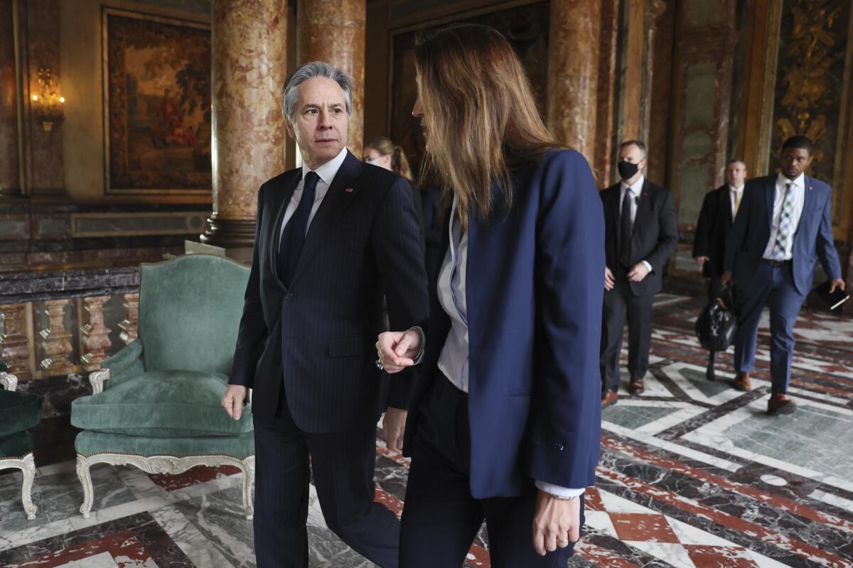 A man, left, and a woman, both wearing business attire, walk side by side in a palace hall