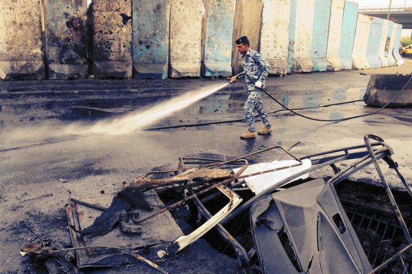 An Iraqi police officer cleans up blood and debris after a car bombing in Baghdad. Seventeen vehicles were incinerated in the deadly attack.