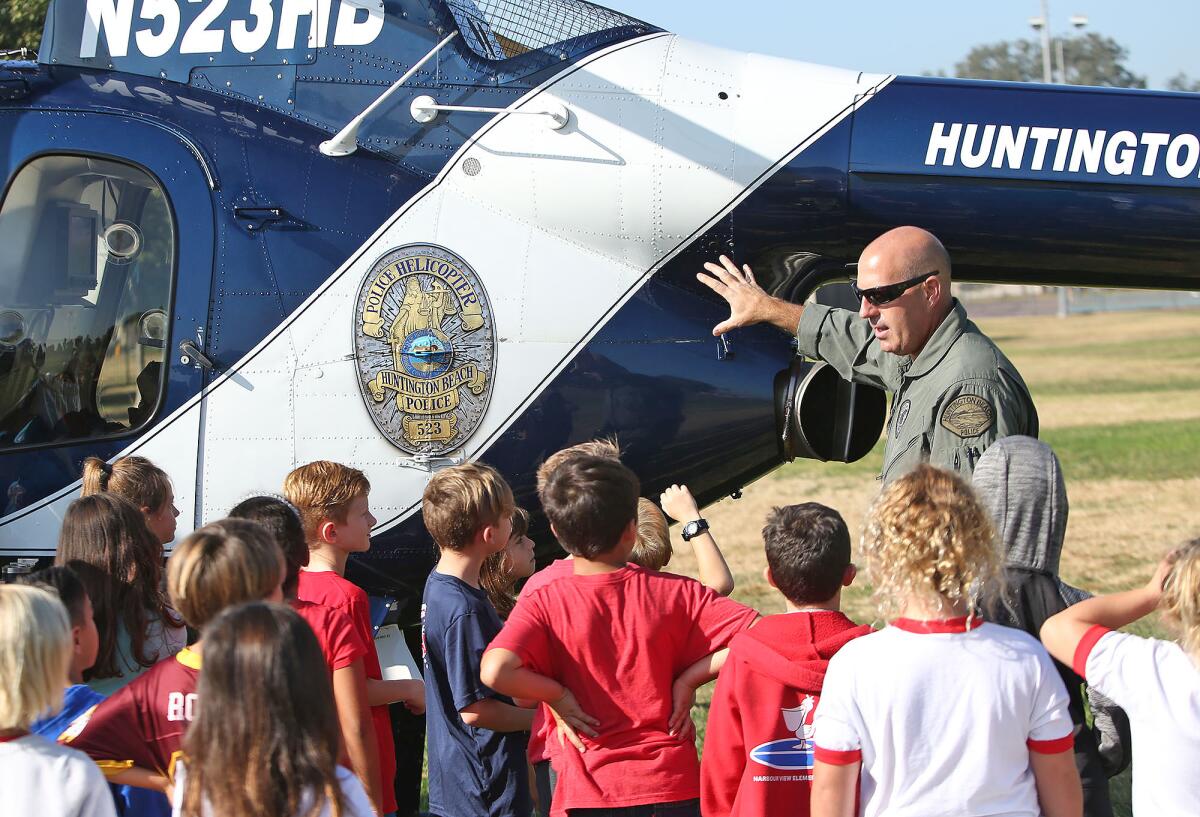 A man in uniform gestures at a parked helicopter while children listen.