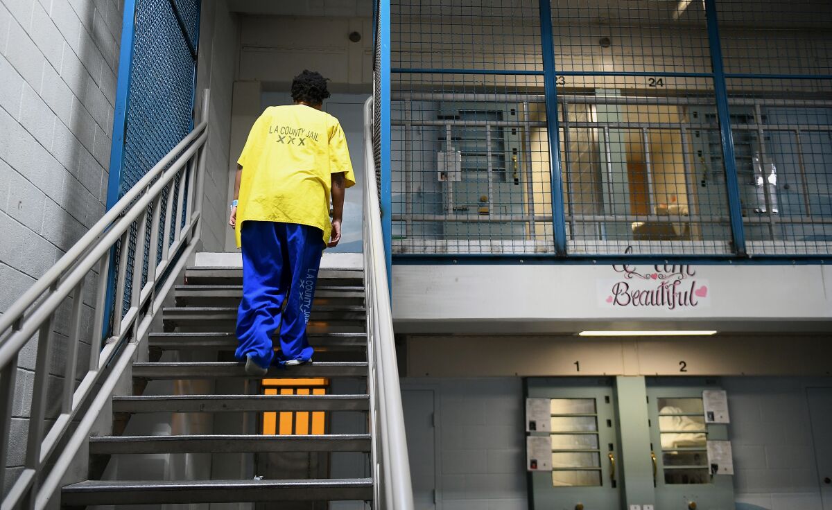 An inmate in yellow pants and a yellow shirt walks up a flight of stairs in jail