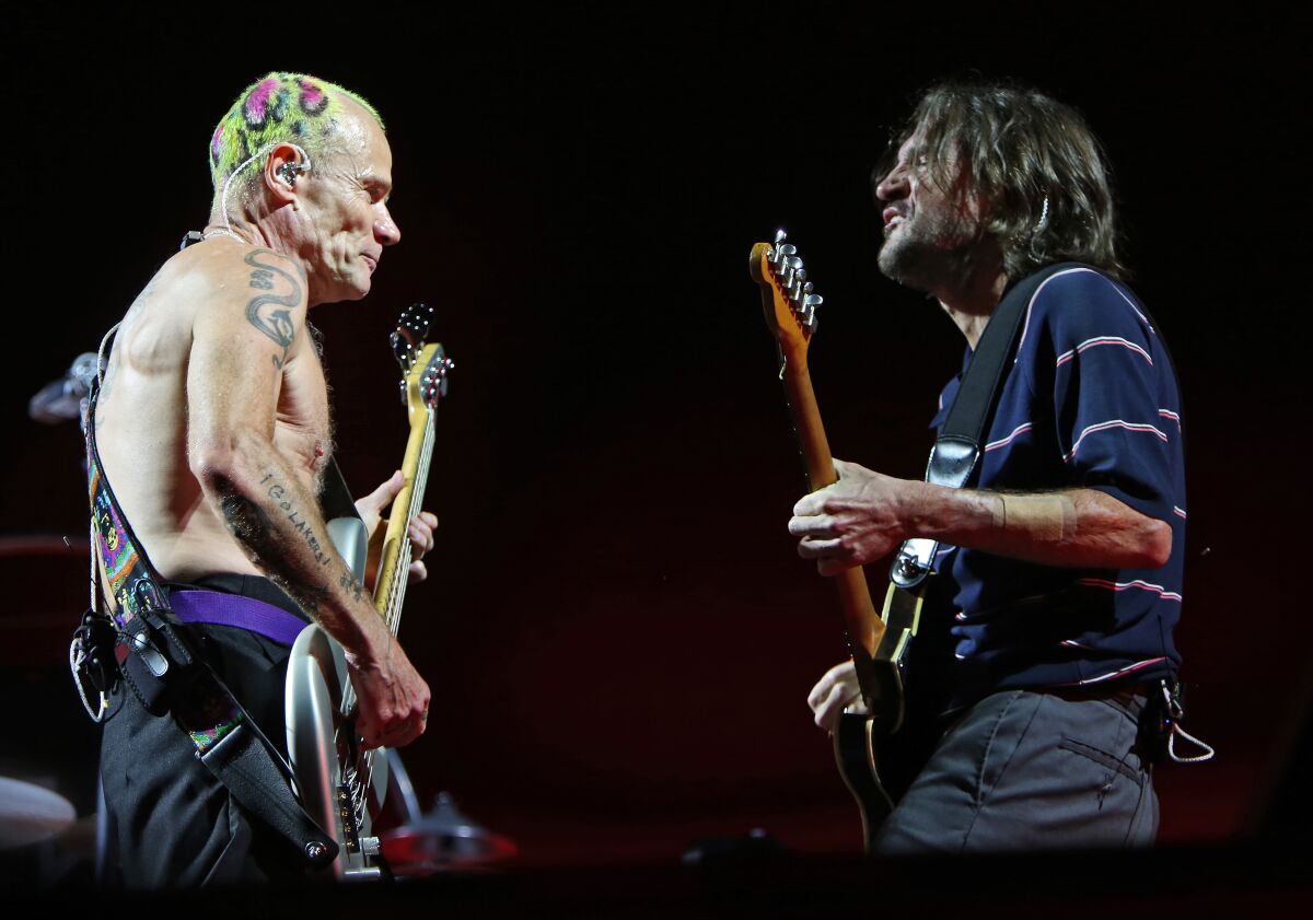 Flea and John Frusciante face each other onstage, instruments in hand.