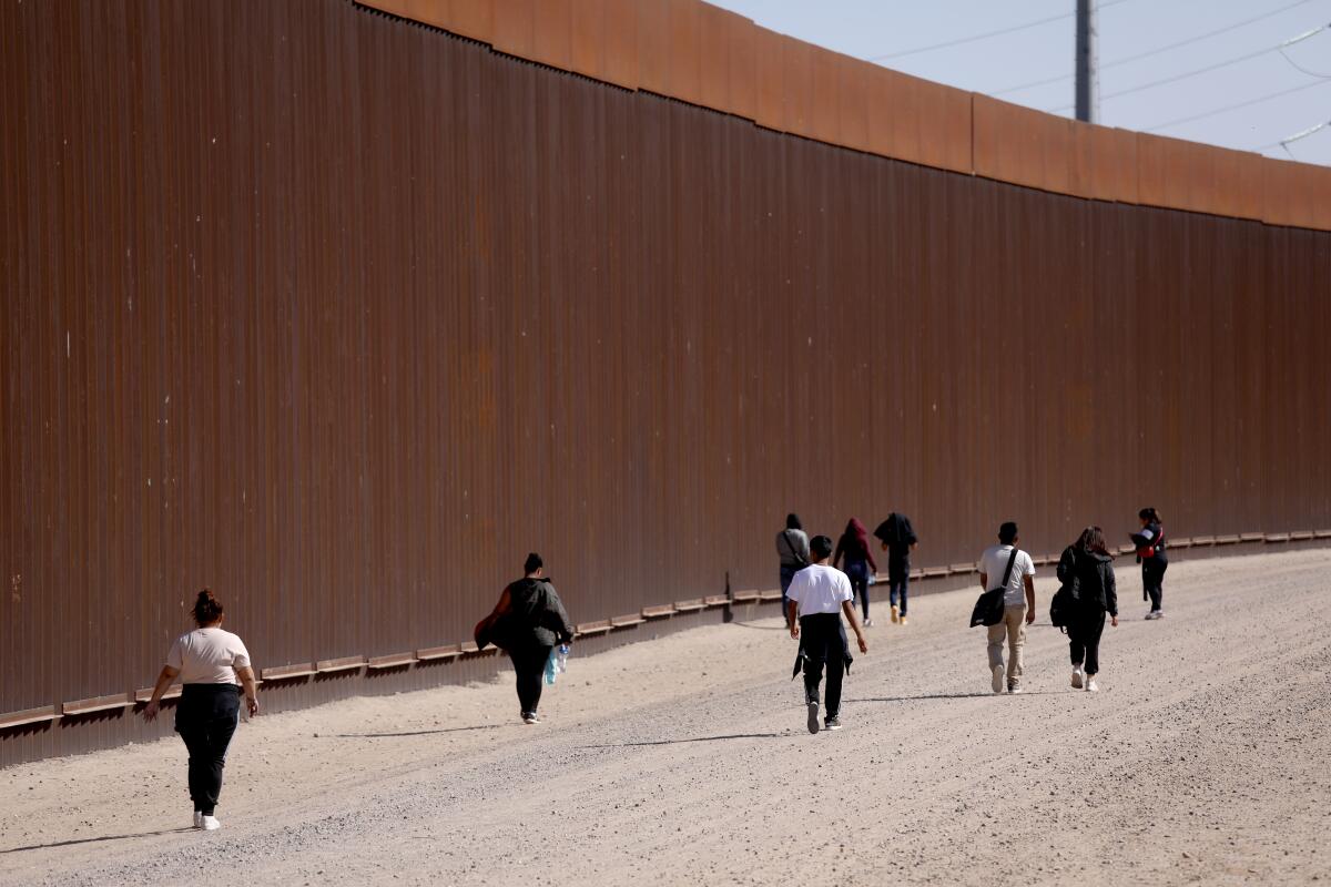 People on a dirt path next to a tall wall 