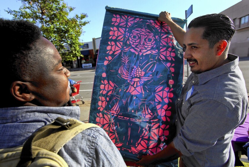 Alfonso Aceves, right, lead artist for L.A. Commons, holds up a papel picado, a traditional Mexican cutout. Students will create an art installation using papel picado bunting for MacArthur Park.