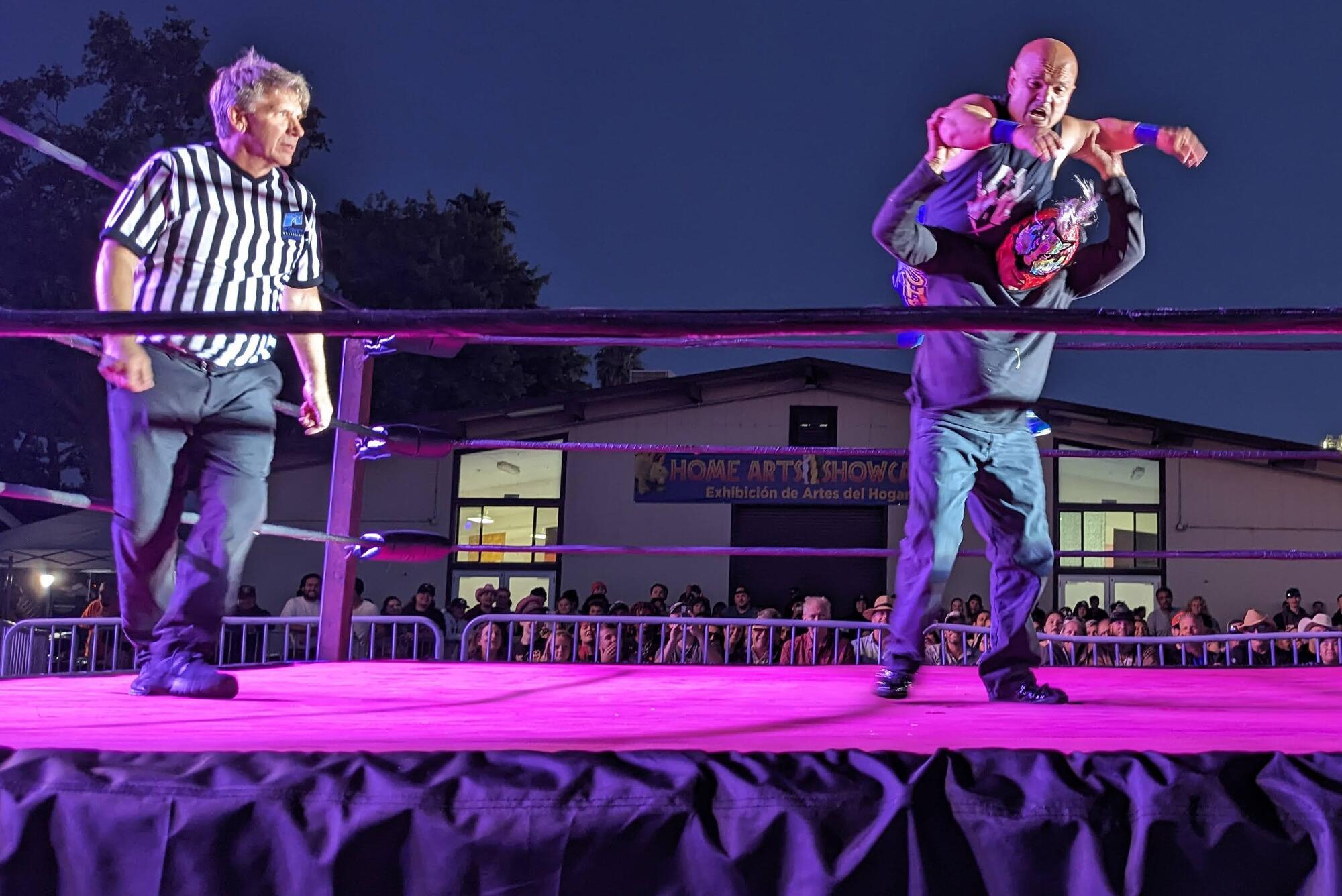 A person is on the back of another person as a referee watches in a ring.