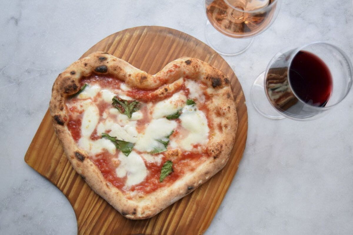 Heart-shaped Neapolitan pizza on a cutting board, a glass of red wine and a glass of rose from La Pizza & La Pasta.
