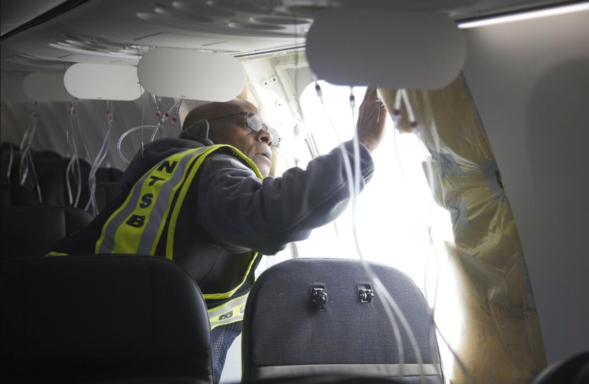 A man in an NTSB high-visibility vest looks at a hole in the side of a jetliner's cabin.