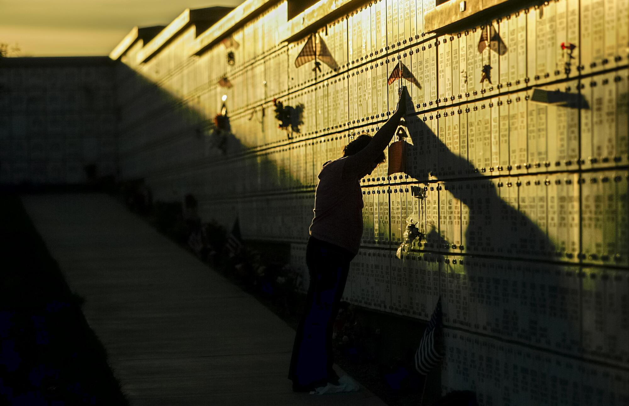 A woman touches a name at a cemetery