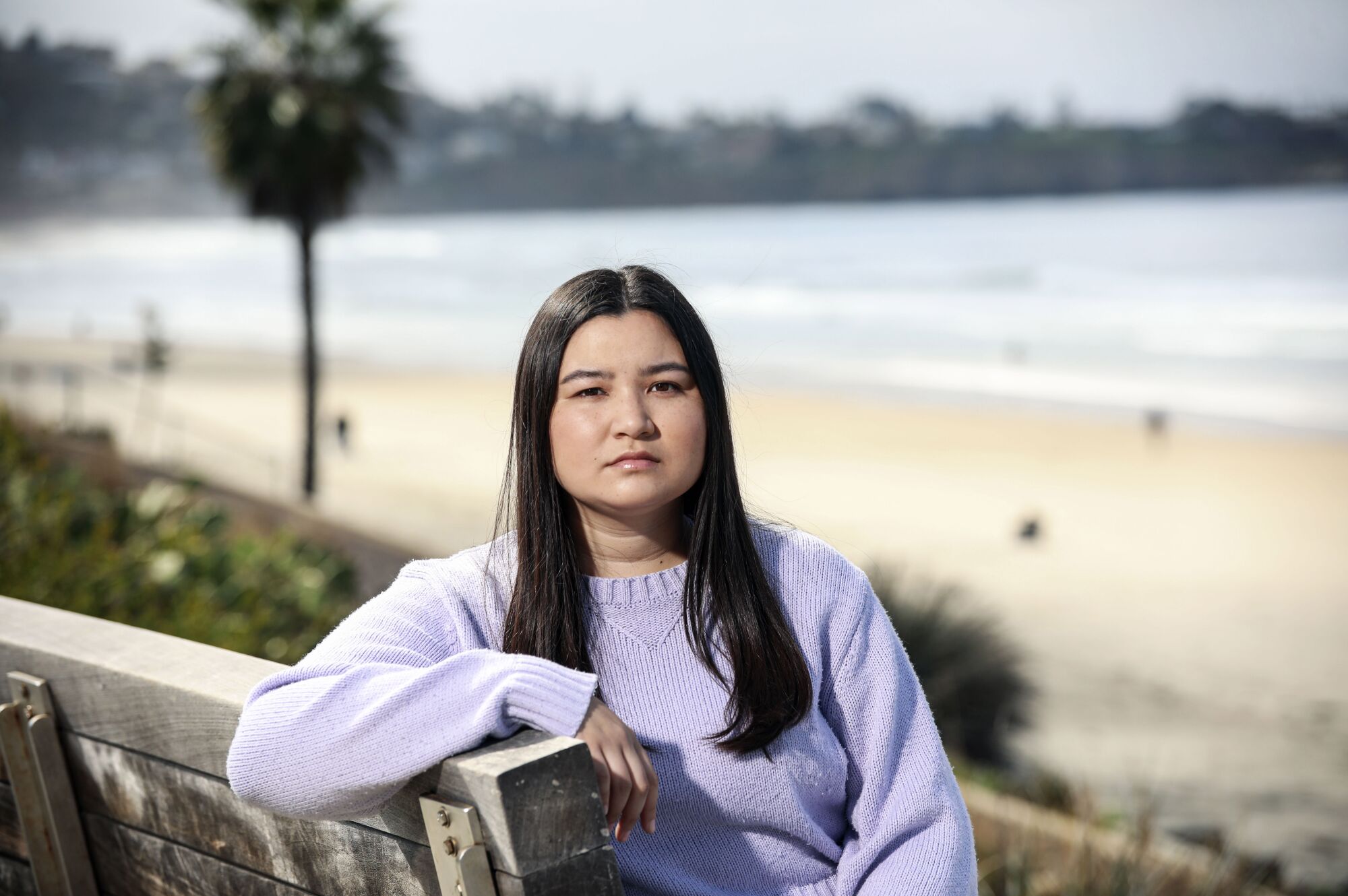 a woman sits on a bench with the ocean behind