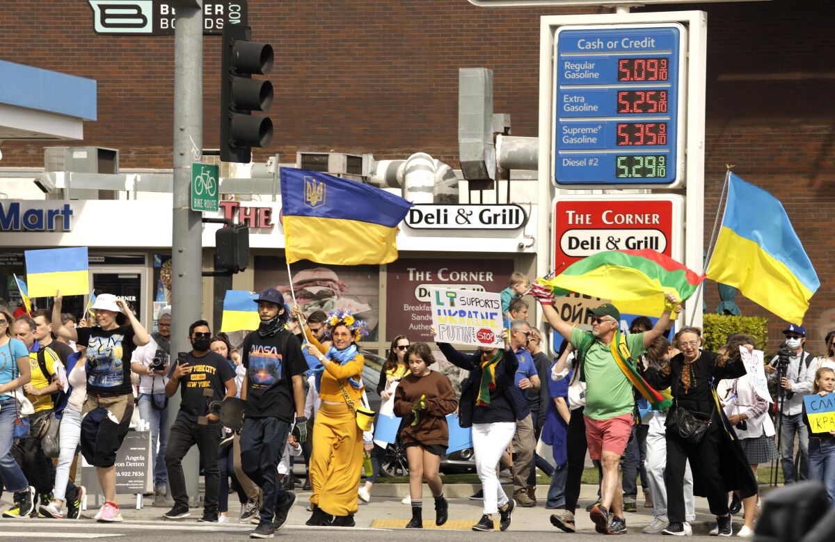 People carrying Ukrainian flags march past a gas station showing prices of $5.09 for unleaded regular and $5.35 for premium