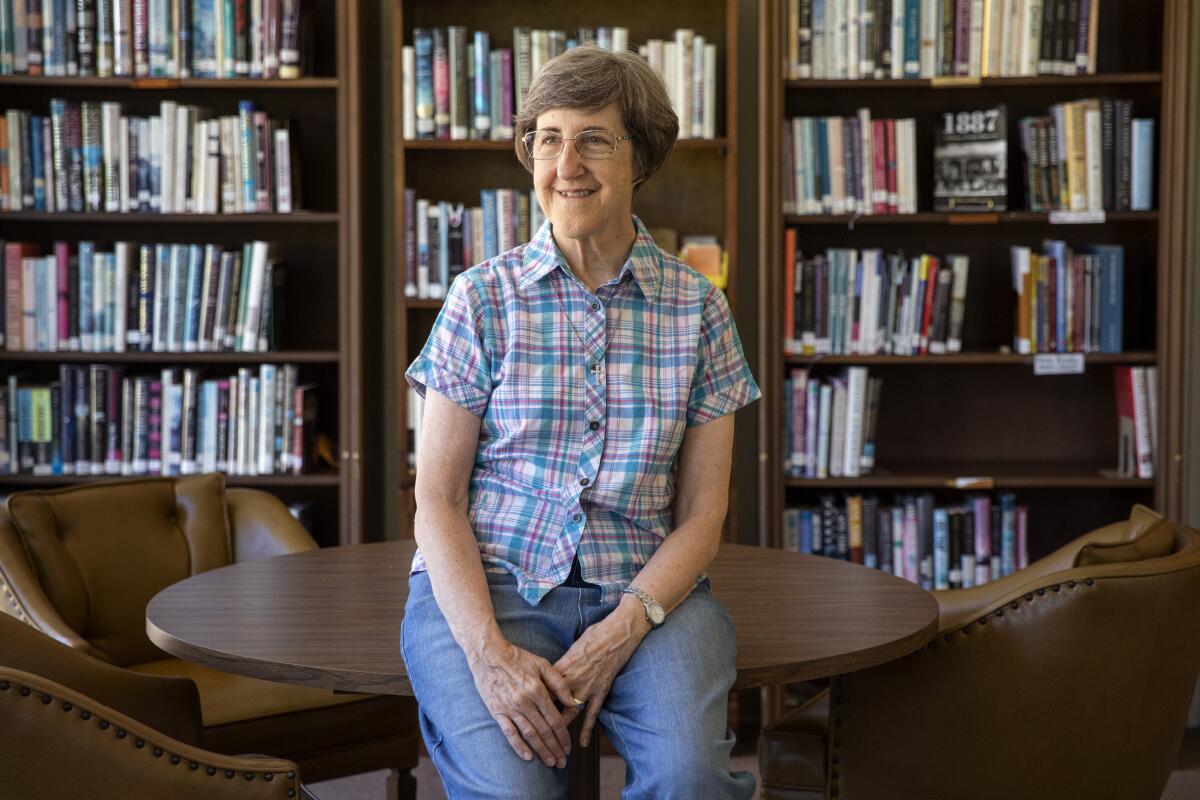 Sister Arlene Trant sitting on a small table in front of shelves of books.