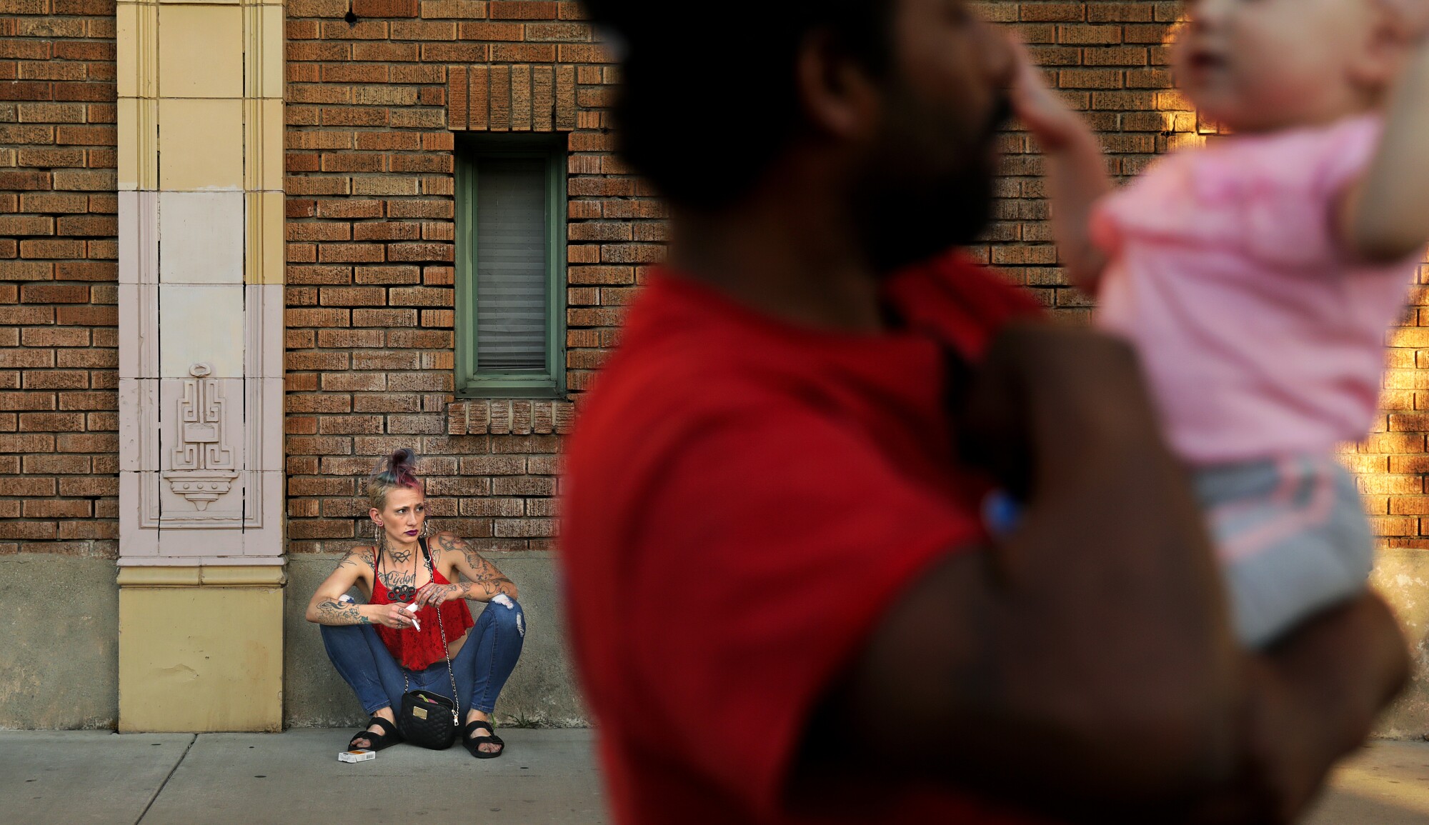 A woman sits against a wall in back as a man holds a baby slightly blurred in the foreground