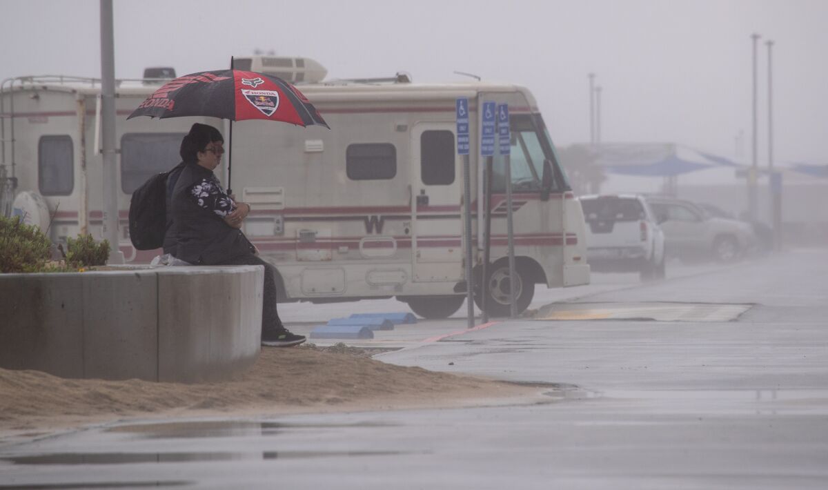 A person sits under an umbrella in heavy rain.
