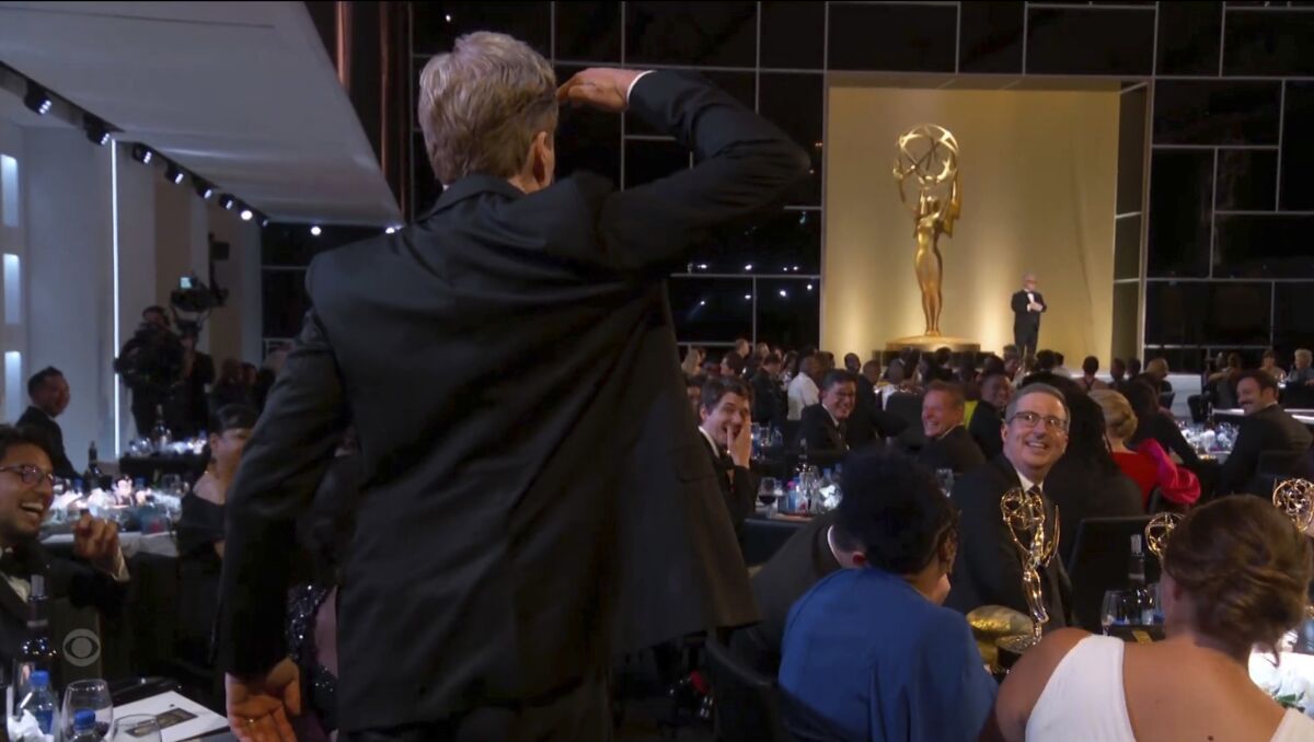A man in a black suit stands up and salutes someone