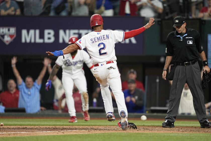 Texas Rangers' Marcus Semien(2) scores on a Nathaniel Lowe single ahead of the throw to the plate as umpire Pat Hoberg, right, looks on in the ninth inning of a baseball game against the St. Louis Cardinals, Monday, June 5, 2023, in Arlington, Texas. (AP Photo/Tony Gutierrez)