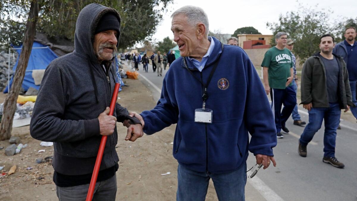 U.S. District Judge David Carter, right, greets a homeless man while surveying a homeless encampment along the Santa Ana River in Anaheim in February.