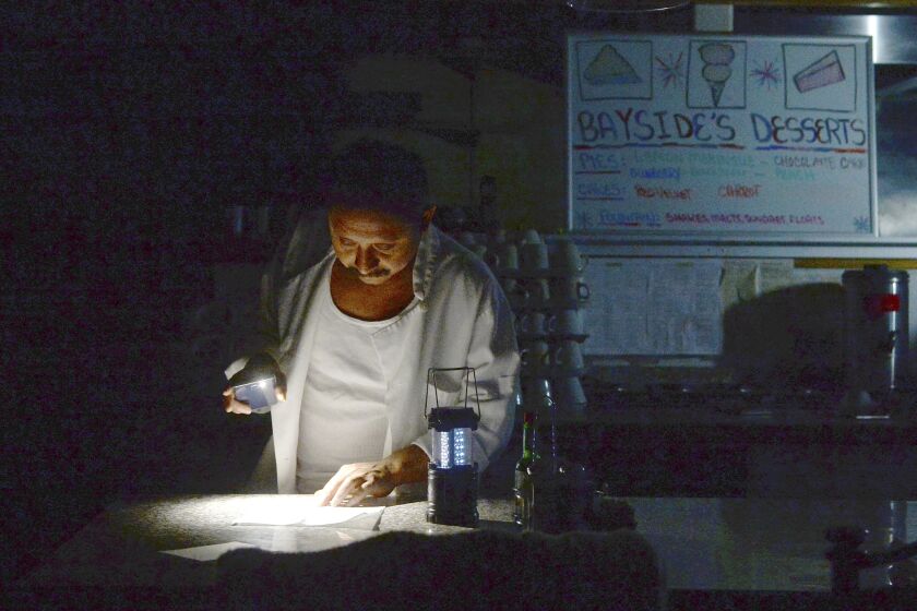 Carlos Lama of Bayside Cafe, which was among businesses to lose power due to PG&E's public safety power shutoff, uses an LED lamp and light from his phone at the counter of the restaurant in Sausalito, Calif., Wednesday, Oct. 9, 2019. More than a million people in California were without electricity Wednesday as the state's largest utility pulled the plug to prevent a repeat of the past two years when windblown power lines sparked deadly wildfires that destroyed thousands of homes. (Alan Dep/Marin Independent Journal via AP)