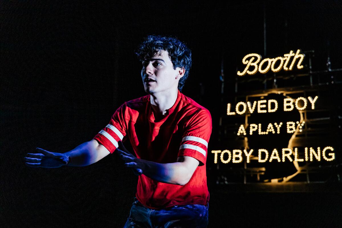 A man stands with arms extended before an illuminated sign reading "Loved Boy: A Play by Toby Darling"