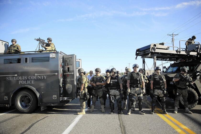 Police officers fortified with an array of military-type equipment stand guard in Ferguson, Mo., where unrest has flared since an unarmed young black man was fatally shot by a police officer.