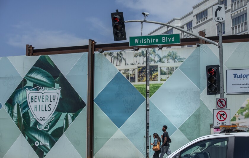 Pedestrians on Wilshire Boulevard. A security camera is above the street sign.