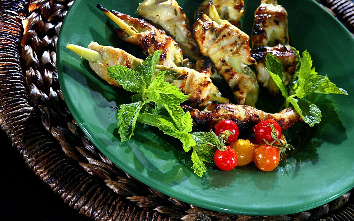 Coconut chicken skewers on a green platter with mint leaves and cherry tomatoes