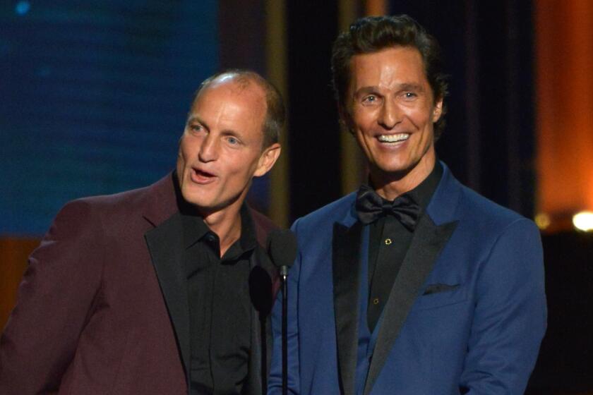 Woody Harrelson wearing maroon suit and Matthew McConaughey wearing blue suit smiling on stage