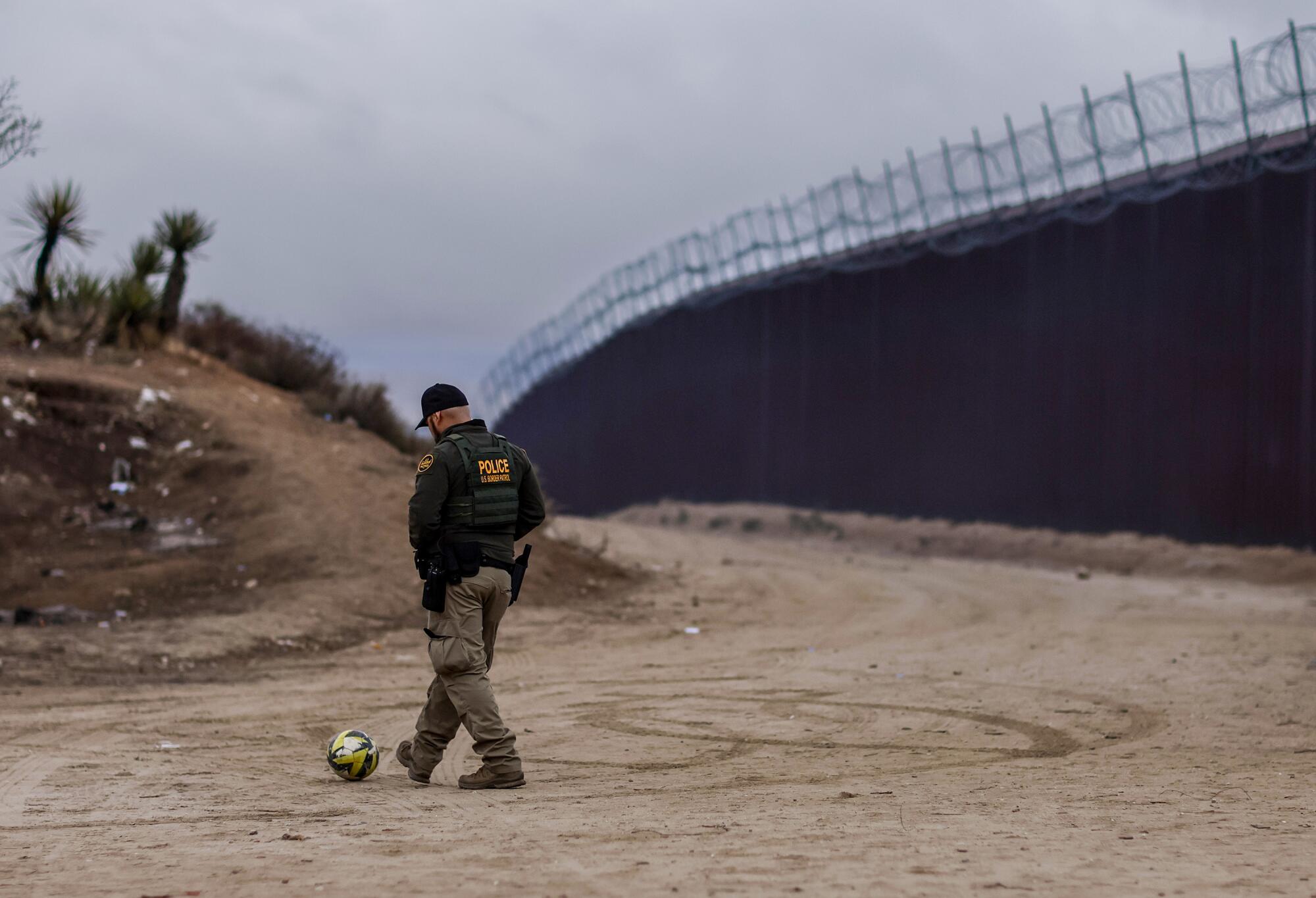 U.S. Border Patrol agent Jorge Perez kicks a soccer ball with asylum seekers at a camp near the border wall.