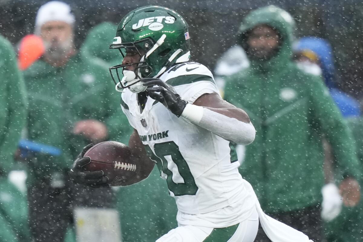 Running back Breece Hall runs with the ball in precipitation.