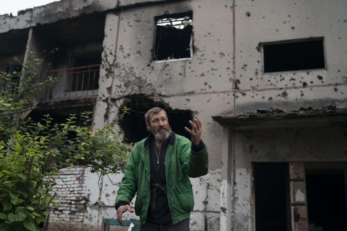 Viacheslav Myronenko, 71, stands in front of the entrance of a damaged building where he lives in the freed village of Hrakove, Ukraine, Tuesday, Sept. 13, 2022. Myronenko has been living in the basement of his bombed-out apartment building with three neighbors for more than four months. (AP Photo/Leo Correa)