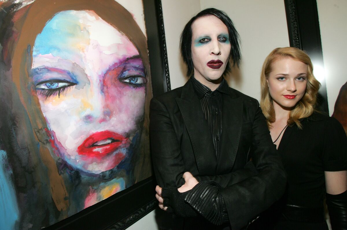 Marilyn Manson in goth makeup stands next to a painting with Evan Rachel Wood
