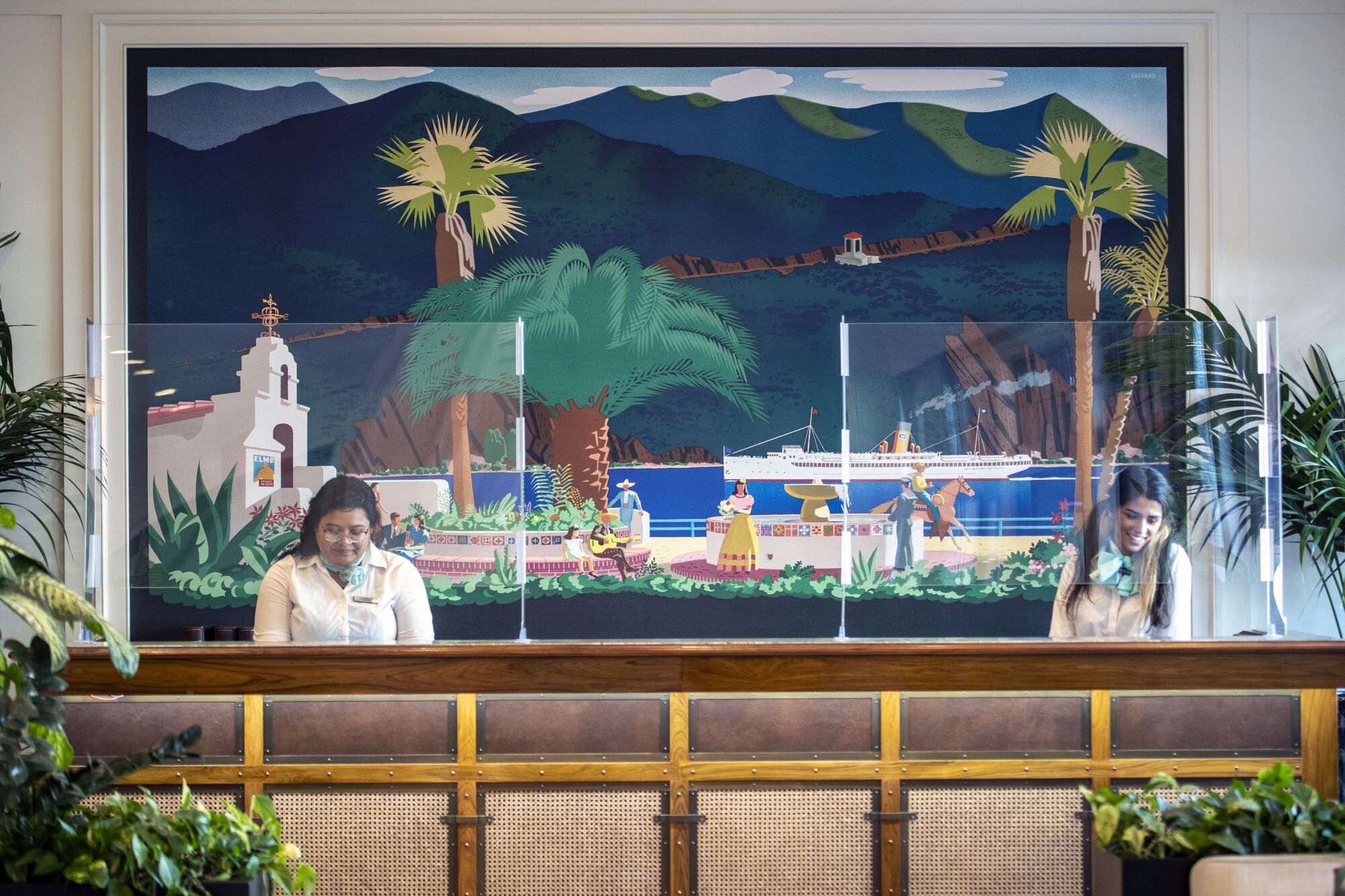 A hotel front counter backed by a mural of palm trees, ocean, a cruise ship and a Spanish Revival-style building