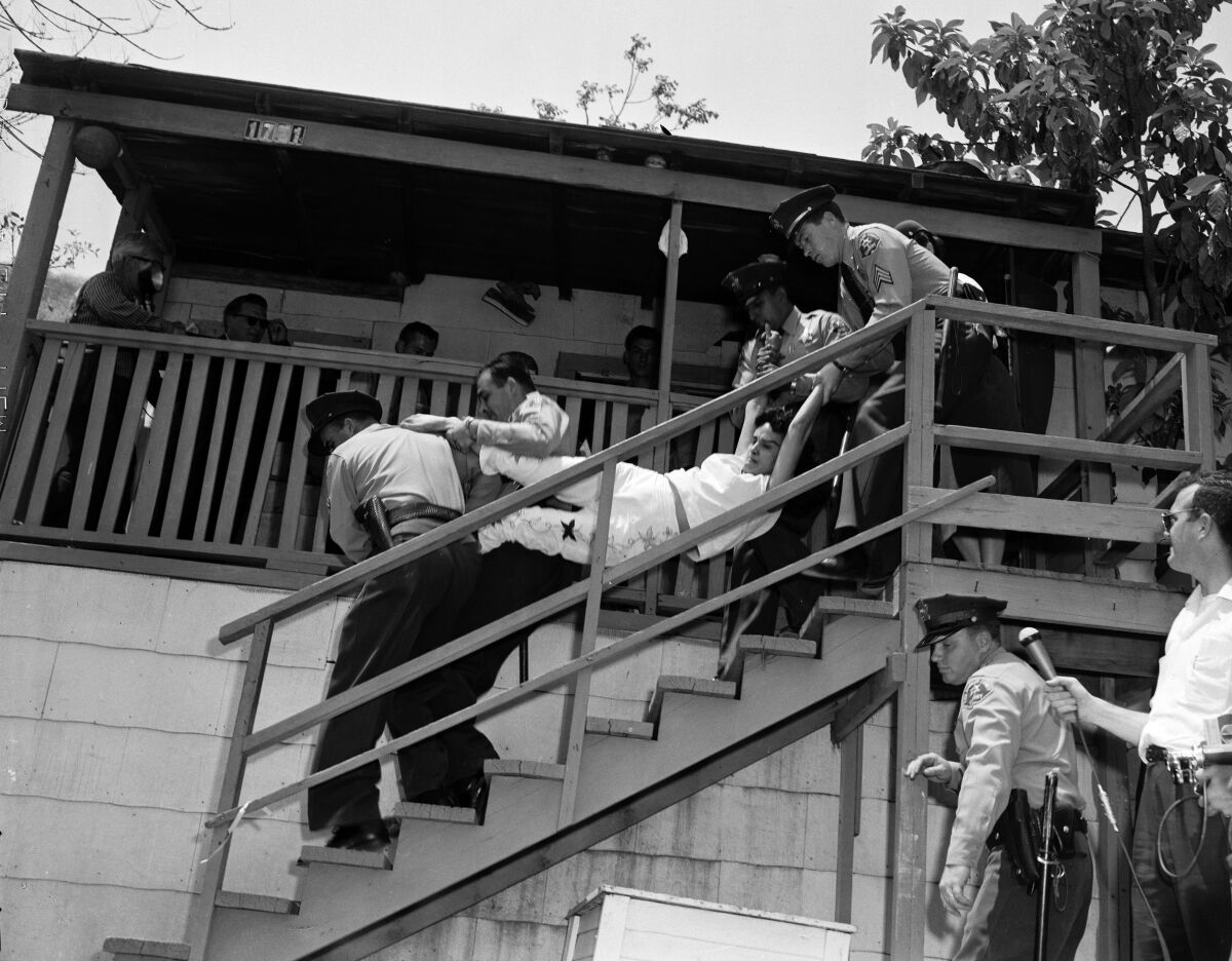 four men in police uniforms carry a screaming woman out of a house
