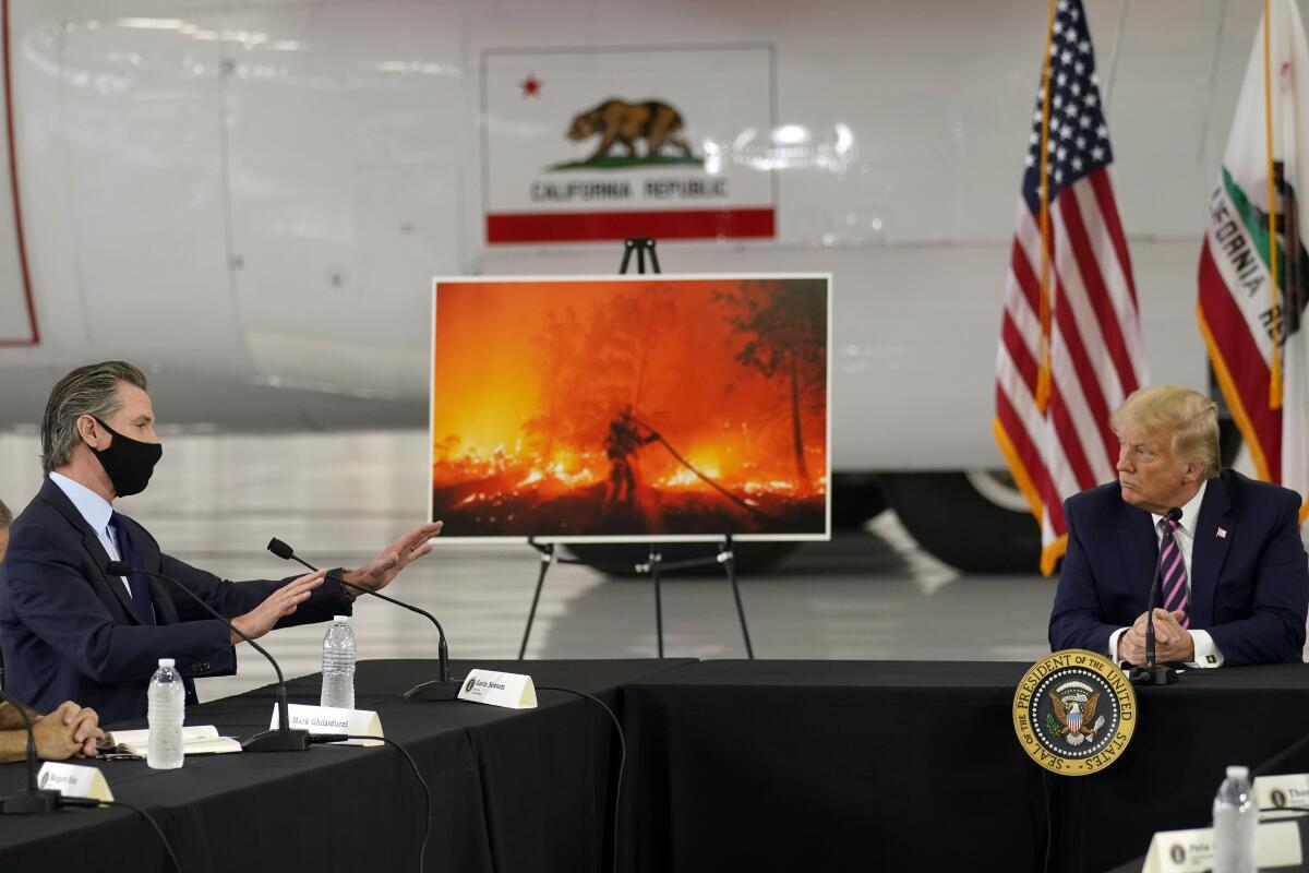 A large image of an orange fire on a stand between Gavin Newsom and Donald Trump as they sit and talk across a large table