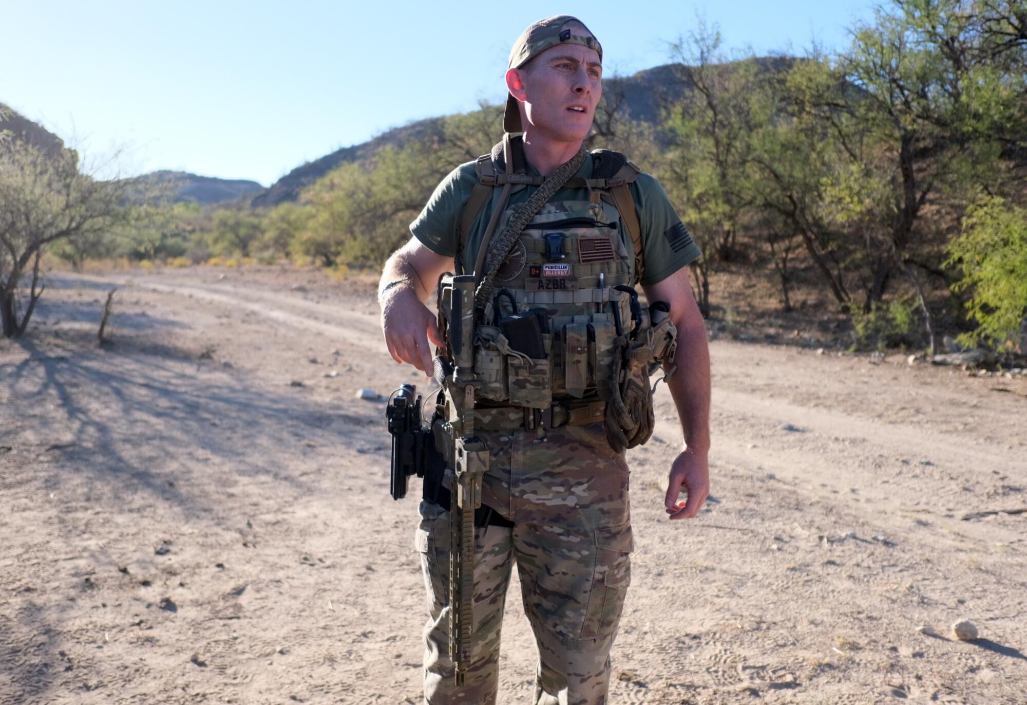 A man wearing camoflage and carring a rifle stands in a desert 