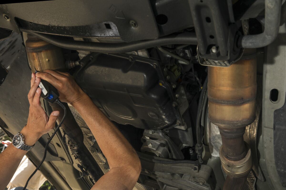 Close-up of hands using a tool to etch numbers into a part underneath a car