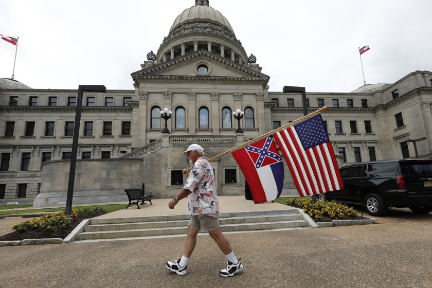 Don Hartness of walks in front of the Mississippi Capitol with a pole carrying the U.S. flag above the state flag