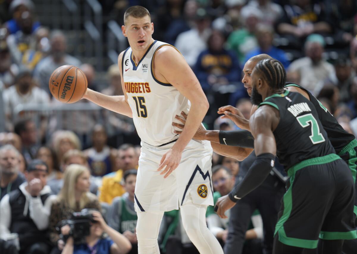 Denver Nuggets center Nikola Jokic, left, looks to pass the ball as Boston Celtics guard Jaylen Brown, front right, and center Al Horford defend in the first half of an NBA basketball game, Sunday, Jan. 1, 2023, in Denver. (AP Photo/David Zalubowski)