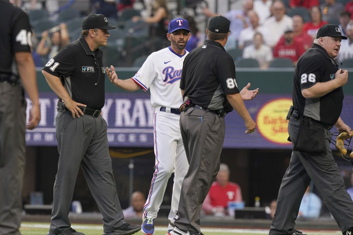 Texas Rangers manager Chris Woodward, center left, questions a call as the umpire crew walks off the field, ending the tenth inning of a baseball game against the Colorado Rockies in Arlington, Texas, Monday, April 11, 2022. The Rockies won 6-4. The crew includes umpires Brian Knight (91), David Rackley (86), Bill Miller (26) and Roberto Ortiz (40). (AP Photo/LM Otero)