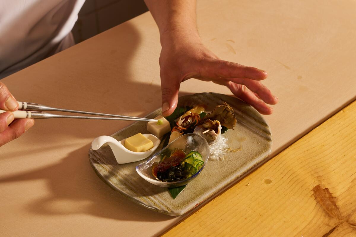 A hand reaches out with a tool to prepare a dish of food.