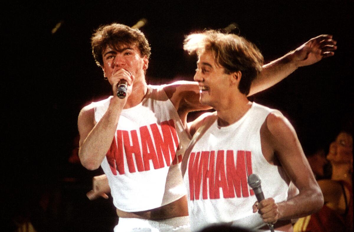 The pop duo Wham!, in matching white t-shirts with the band's name across them, performs onstage.