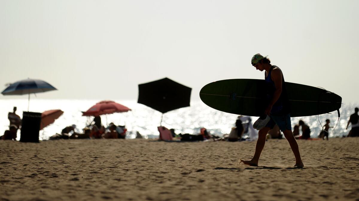 A surfer walks through the sand near the Huntington Beach Pier.