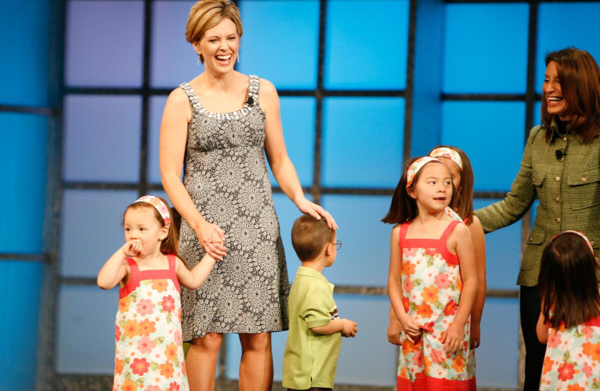 A woman in a gray dress stands with several young children on a stage. 