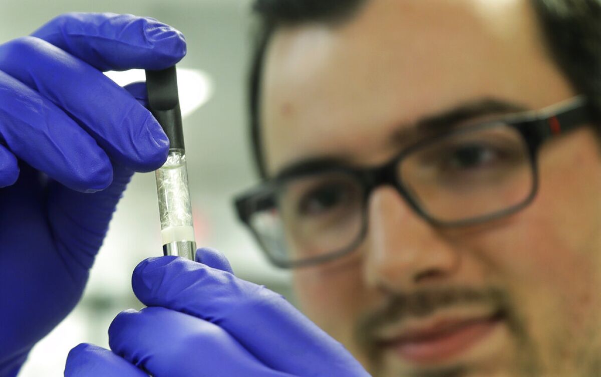 A lab worker holds a vape cartridge 