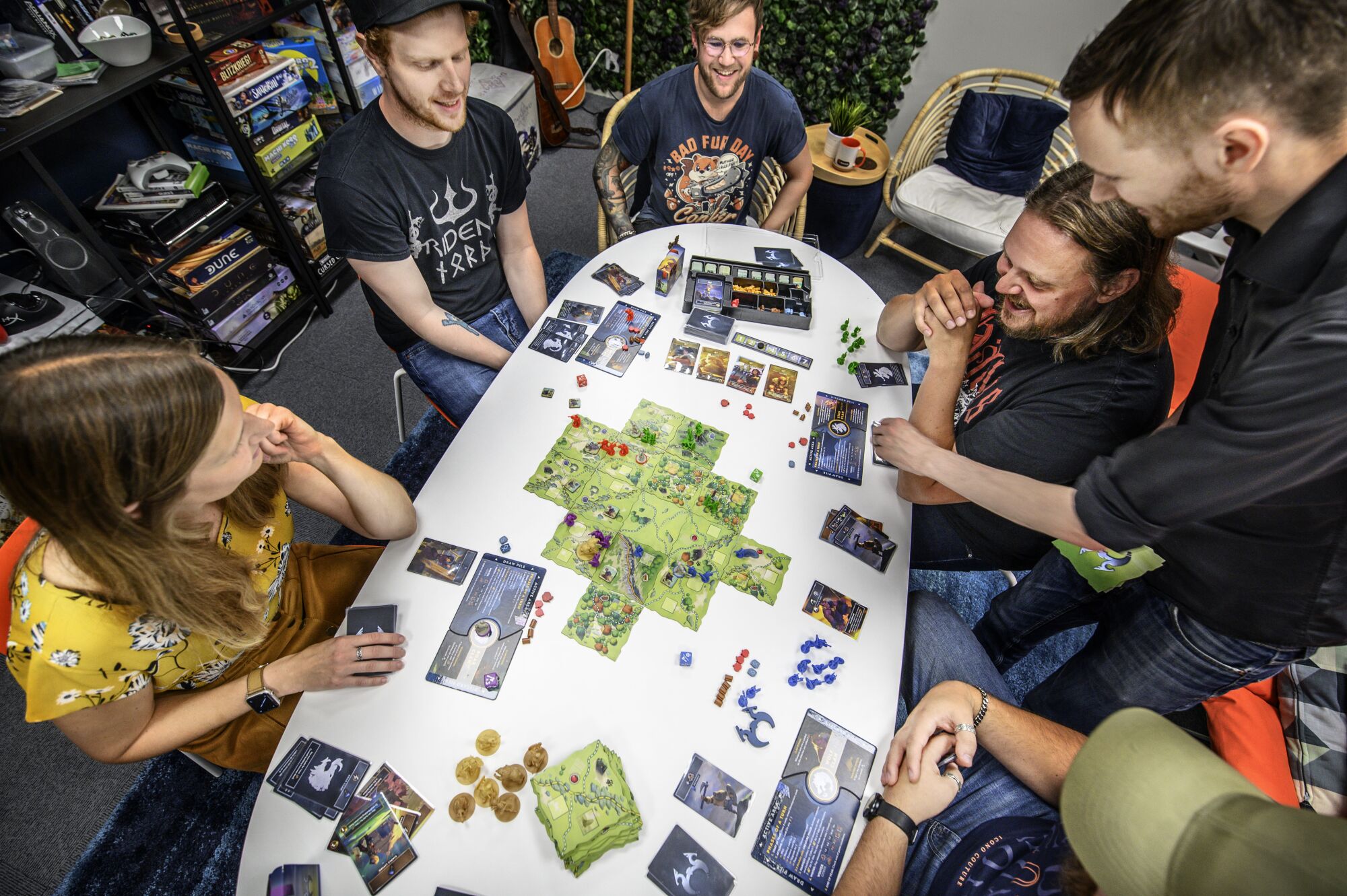 Vue de dessus d'une femme et de trois hommes, certains souriants, assis autour d'une table regardant un jeu de société