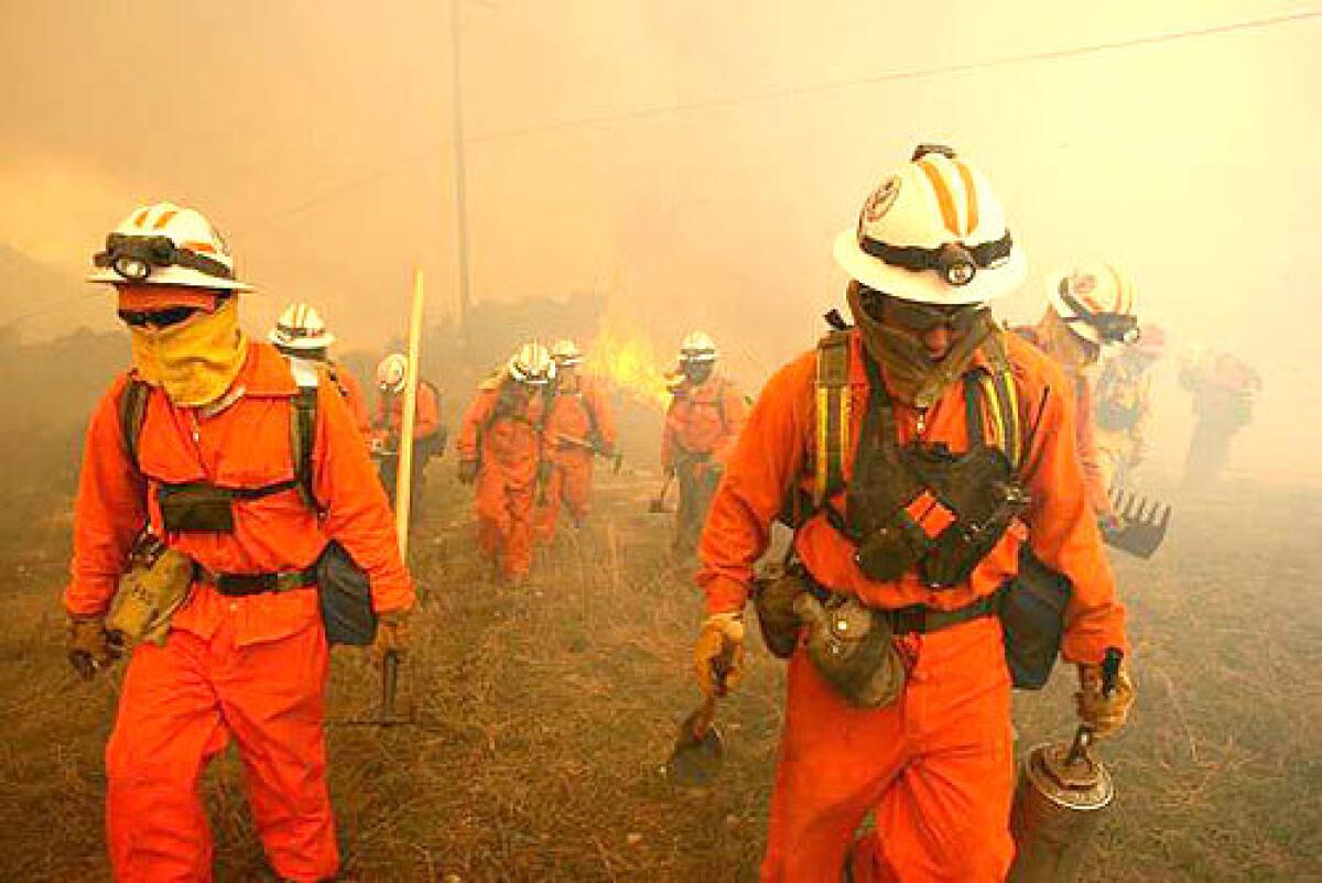 ON THE LINE: Inmate crews with the California Department of Corrections help fight the wind-whipped blaze that has blackened more than 6,500 acres in eastern Orange County. Nearby residents have been allowed to return home, but a major toll road remains closed.