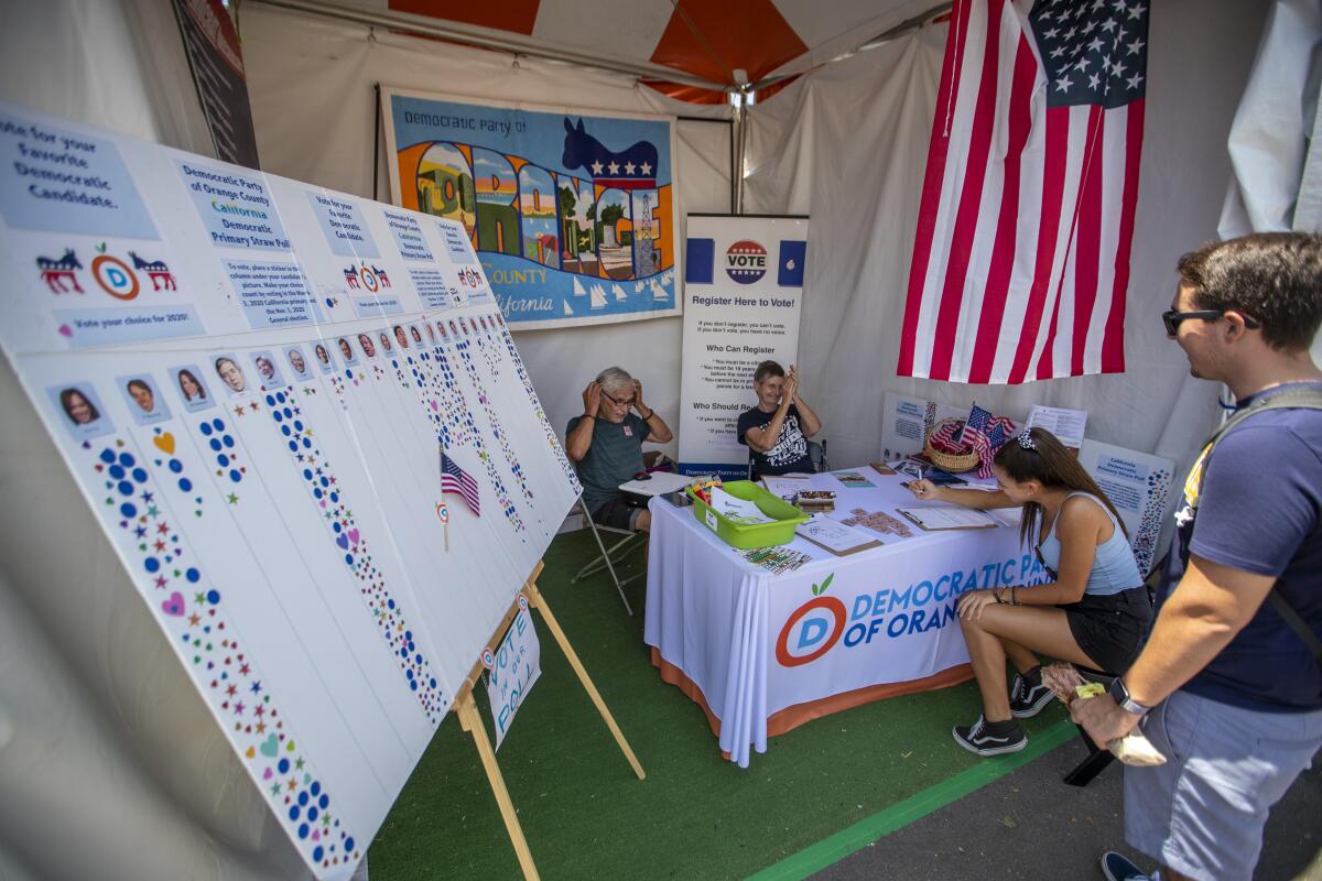 Dr. Nick Hernandez, left, and Mary Carter, center, volunteers with the Laguna Beach Democratic Party, register Sydney Magno, of Riverside, to vote as a democrat with her friend, Daniel Sosa, at the Democratic Party of Orange County booth at the Orange County Fair in Costa Mesa, Calif.