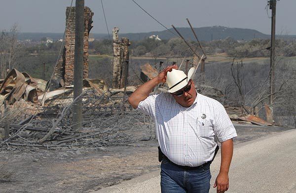 Palo Pinto County Sheriff Ira Mercer holds onto his cowboy hat as the wind picks up during a tour of the fire-ravaged area.