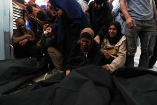 People, some kneeling, grieve before black body bags